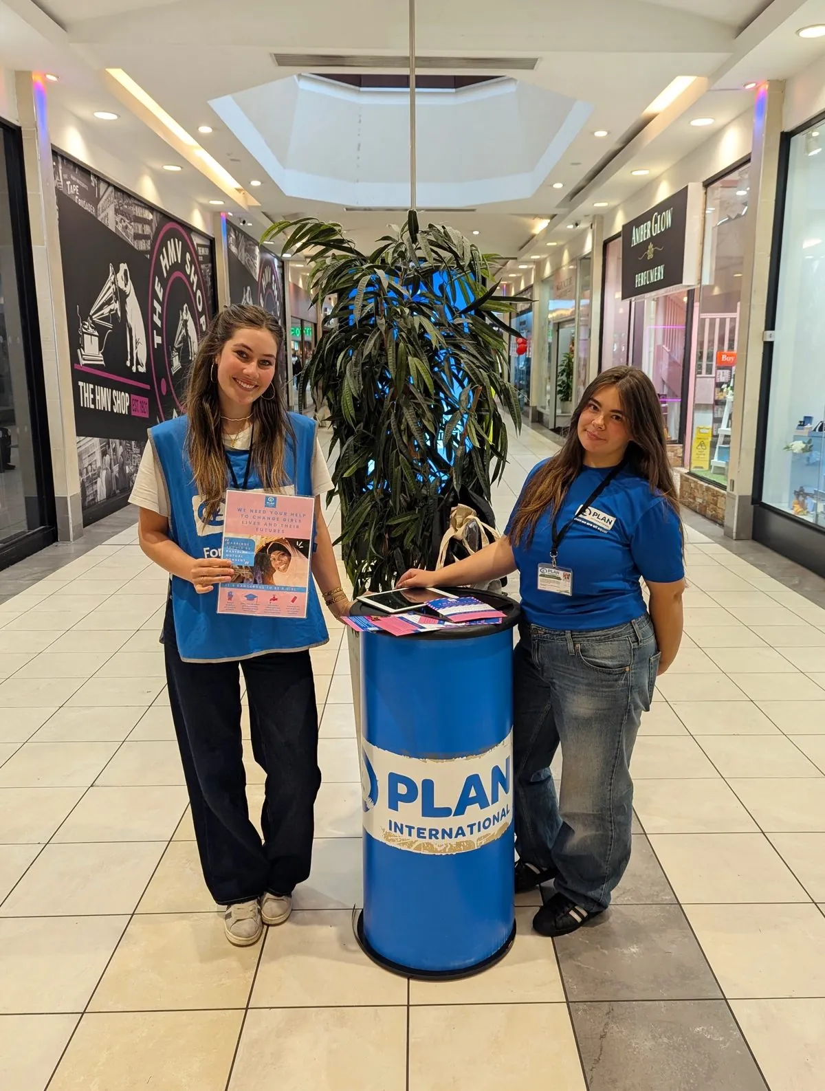 Two Plan International fundraisers beside a branded stand in a shopping centre