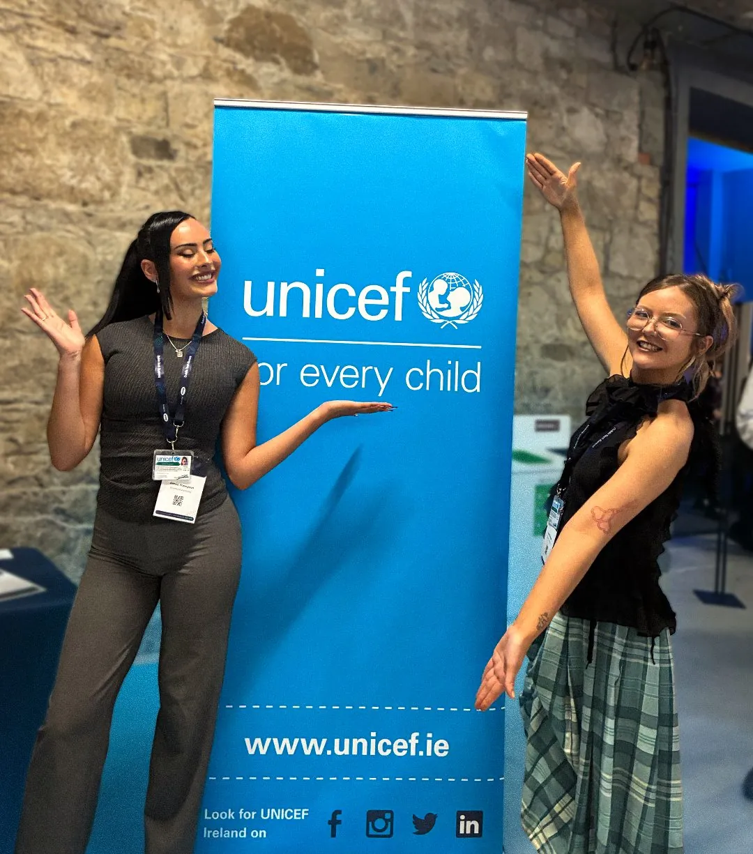 Two UNICEF fundraisers posing beside a UNICEF banner at an event