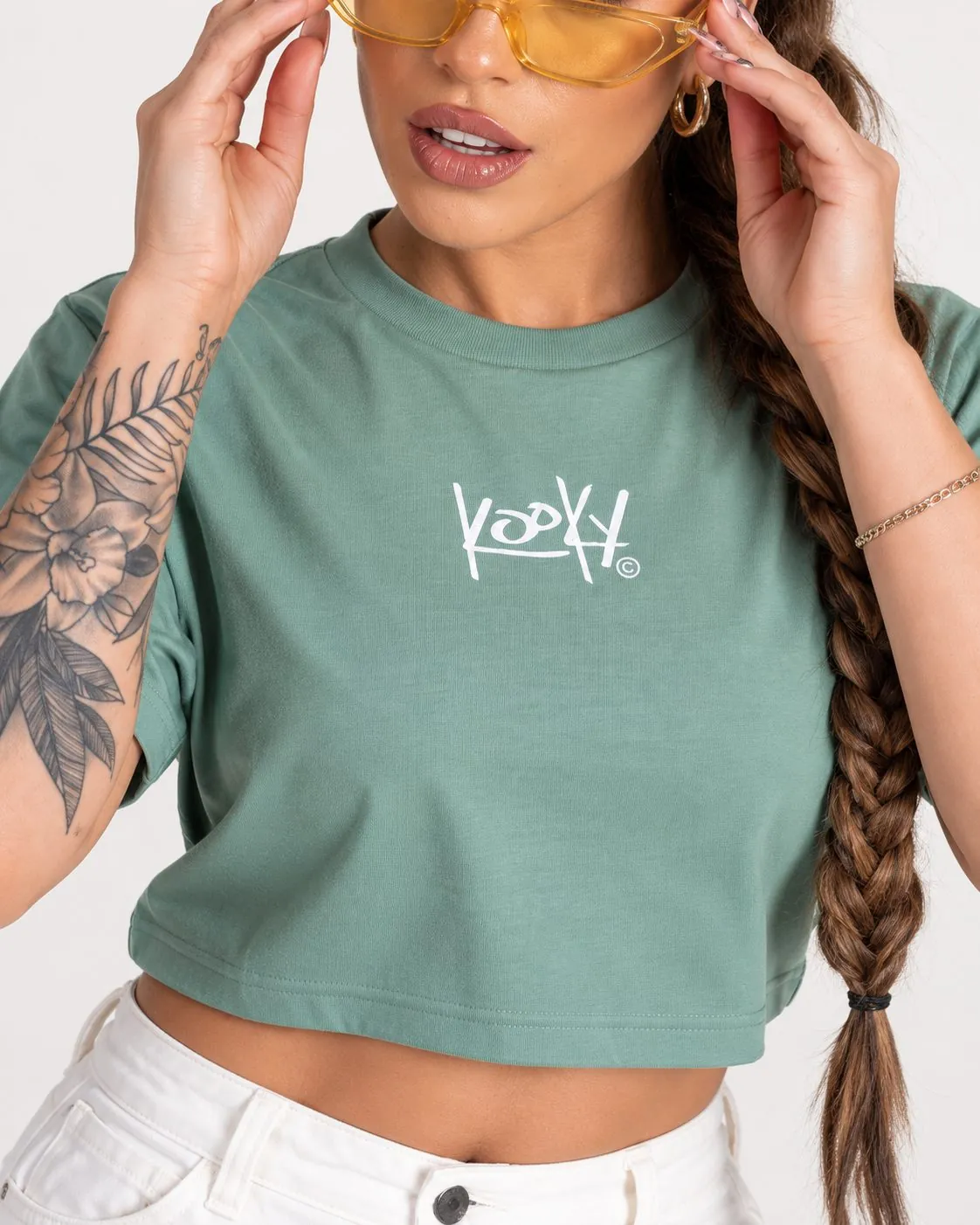 Close-up of a sage green Kooky cropped T-shirt with the white Kooky wordmark