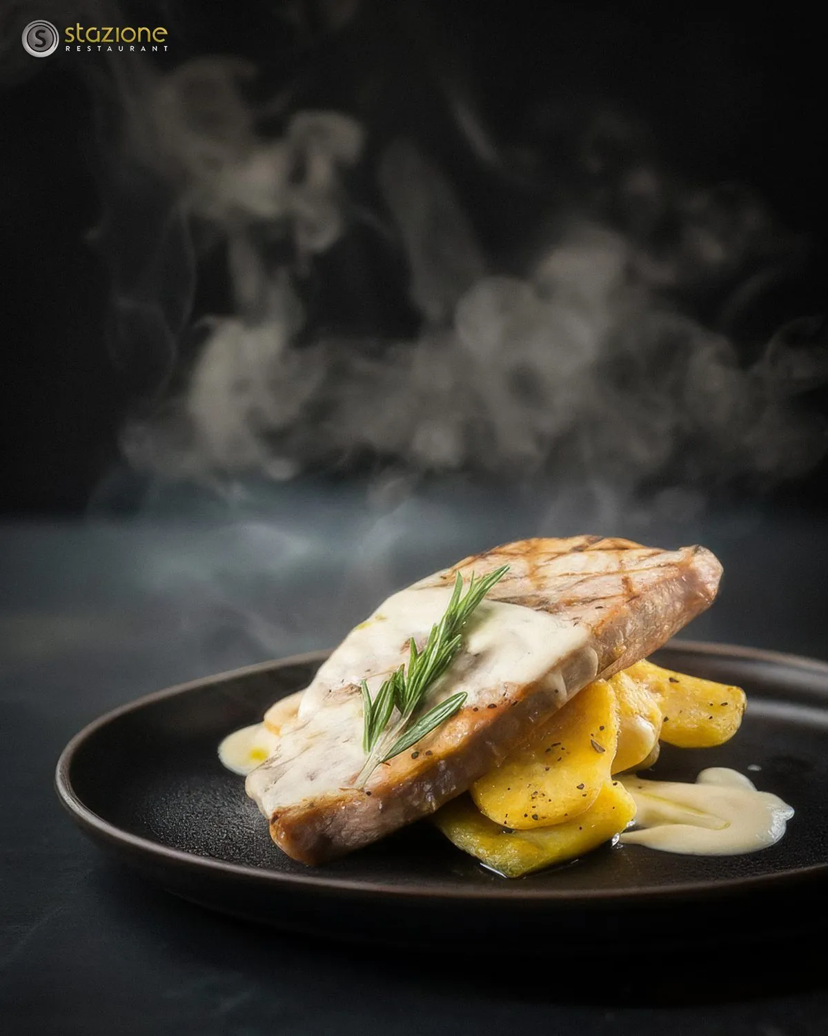 Steaming grilled fish with rosemary and sliced potatoes on a dark plate
